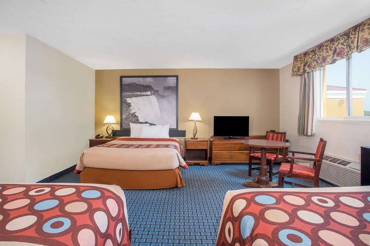 A hotel room with two beds, a desk, a chair, a TV, and a large window with curtains.