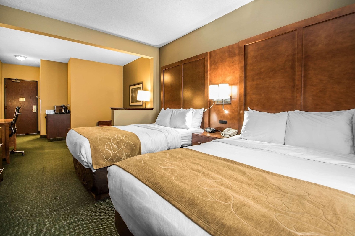 A hotel room with two beds, a desk, a chair, a coffee machine, and a telephone.
