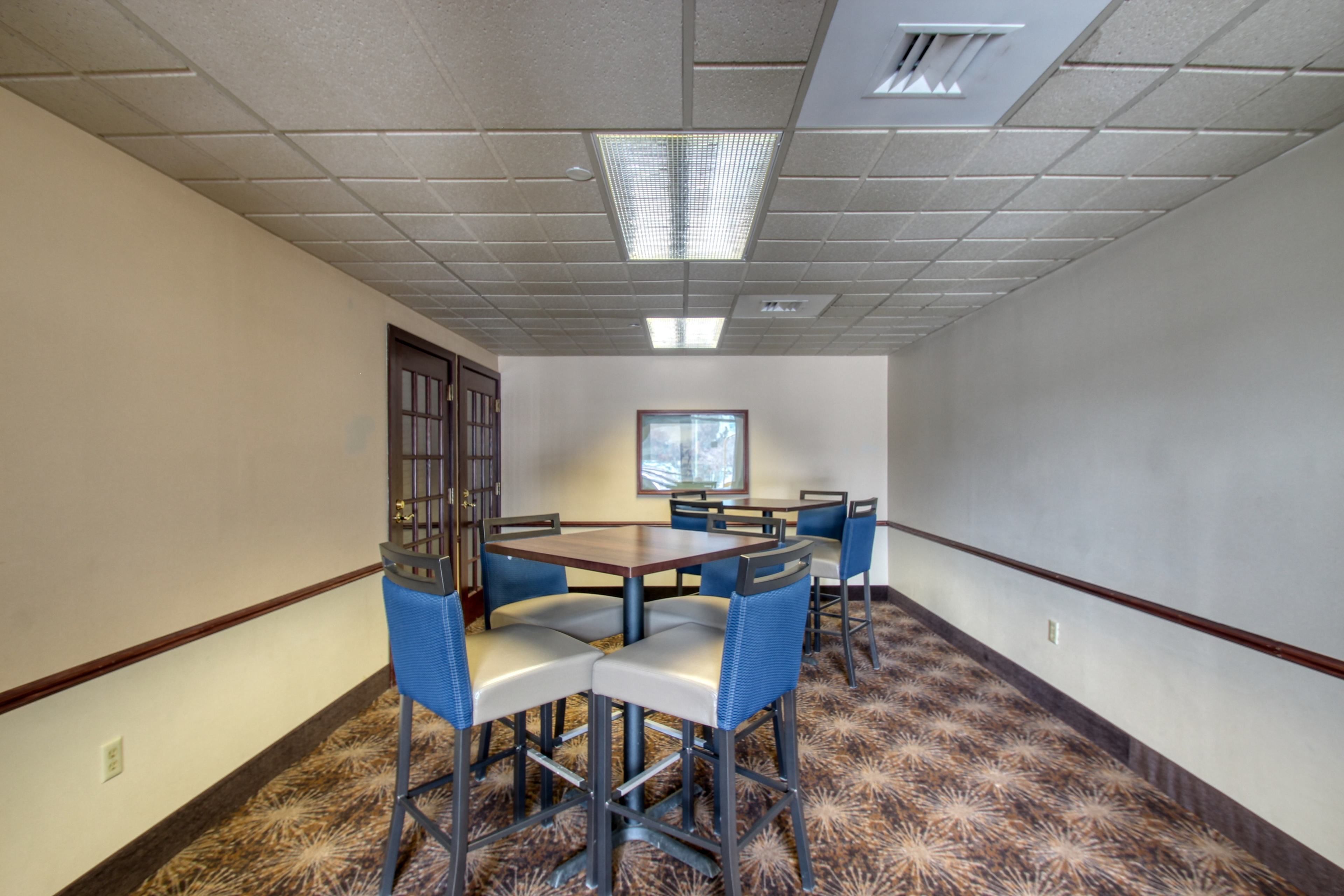 Une salle de conférence avec une grande table et six chaises, une porte, une fenêtre et un tapis à motifs.