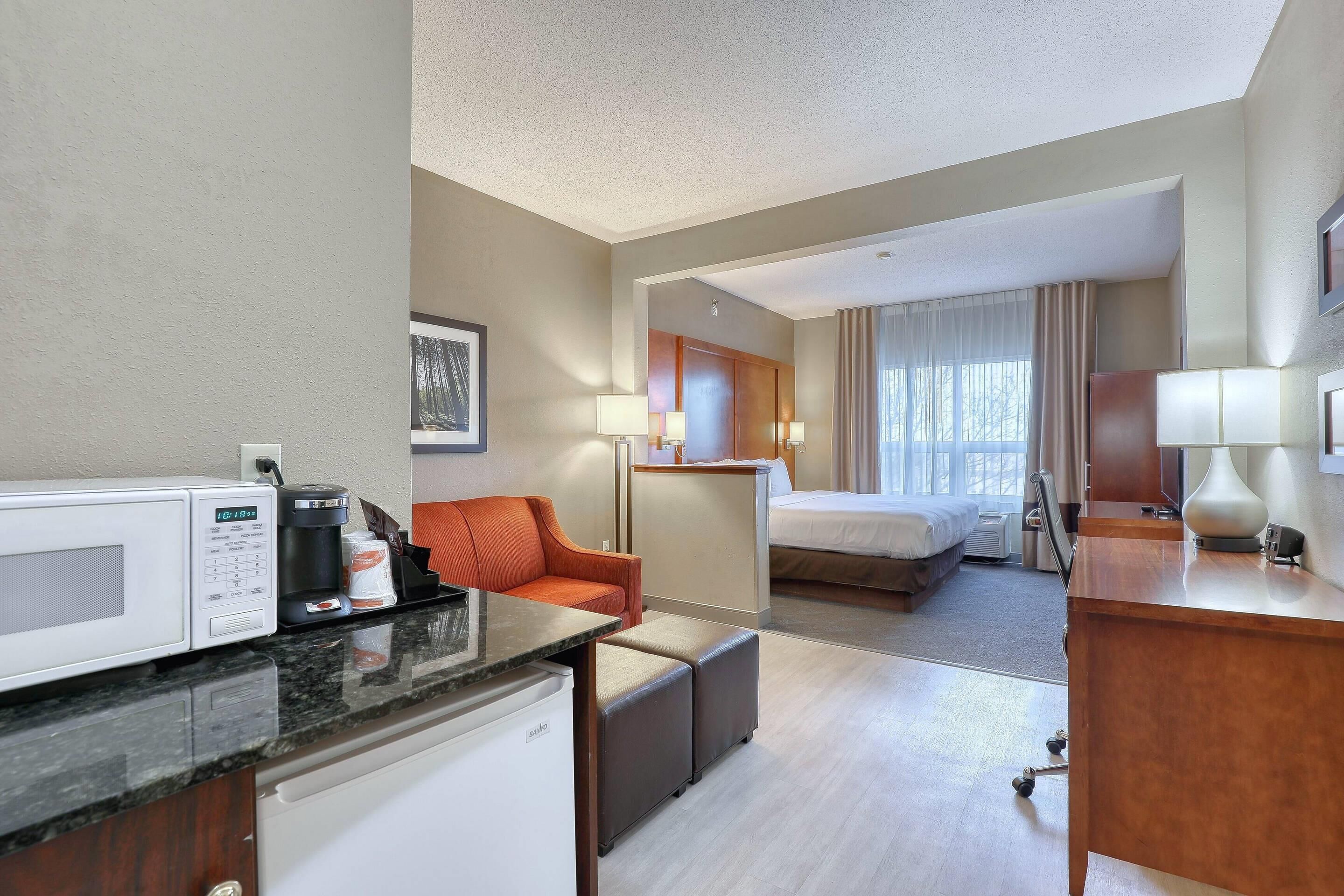 A hotel room with a kitchenette, a bed, a desk, and a seating area.