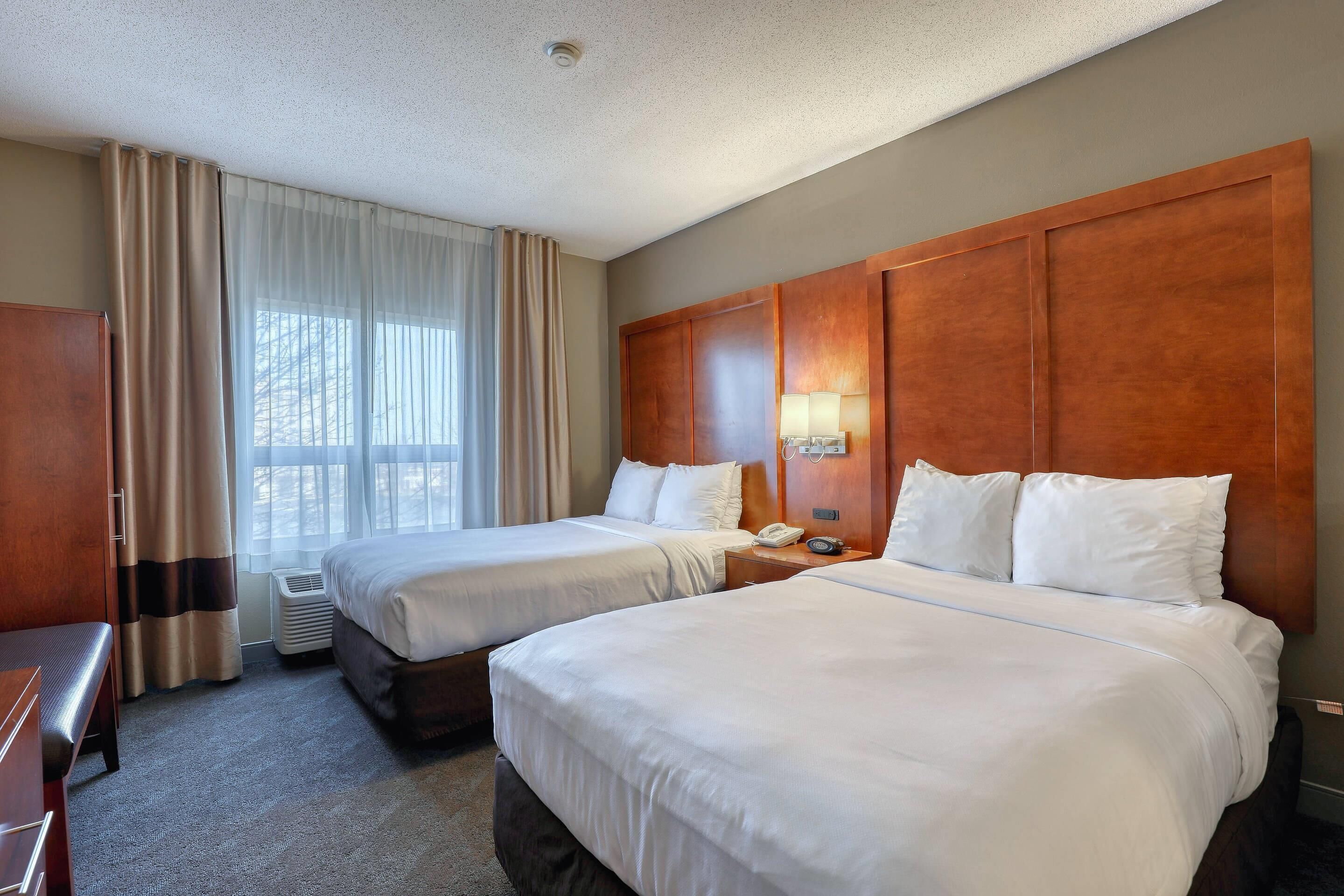 A hotel room with two beds, a desk, a lamp, and a window with curtains.