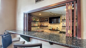 Un espace bar doté d’un comptoir en granit, de tabourets de bar et d’une variété de bouteilles d’alcool.