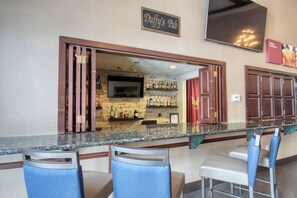 Un espace bar avec un comptoir, des tabourets de bar et un téléviseur fixé au mur.