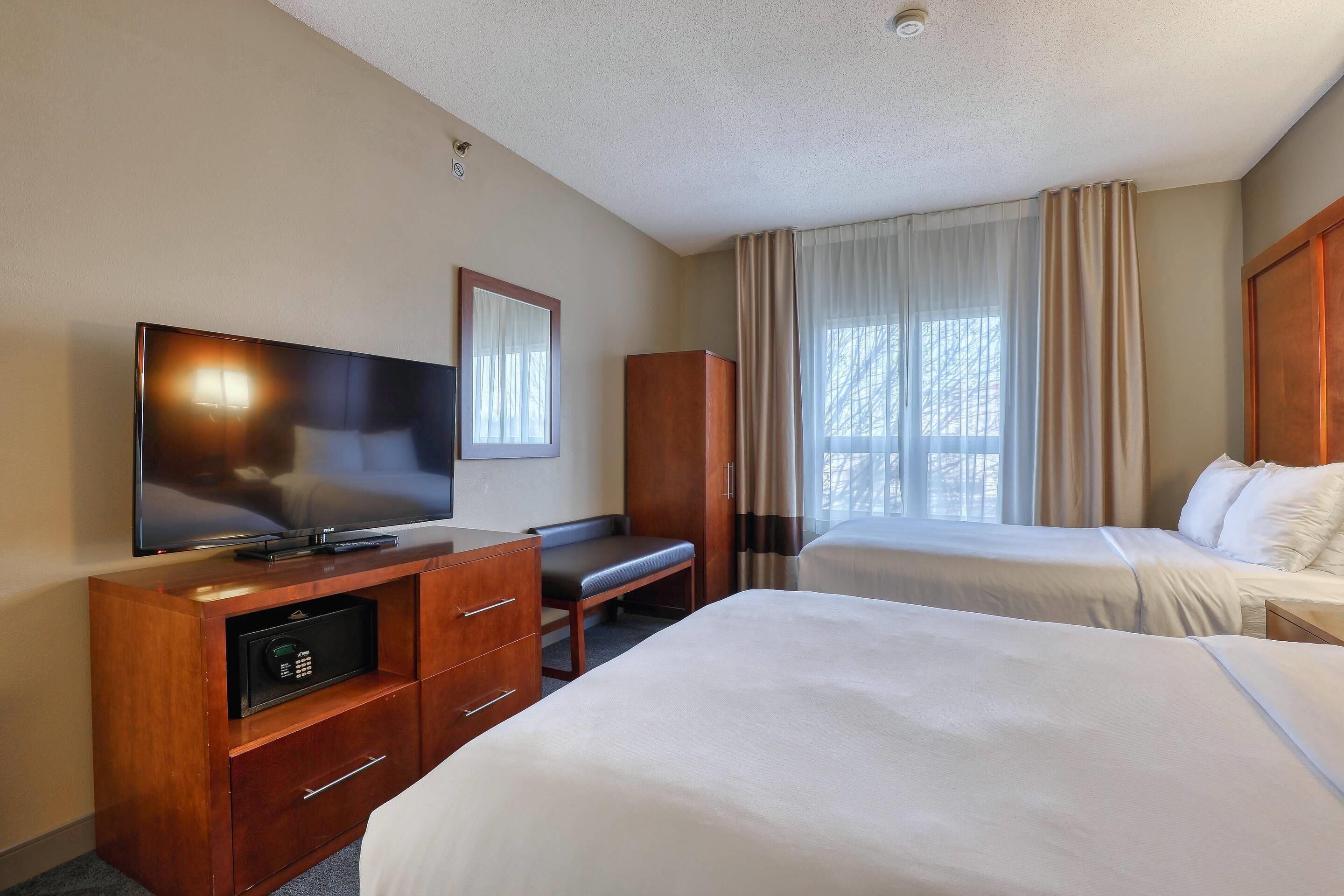 Ein Hotelzimmer mit Fernseher, Schreibtisch, zwei Betten und einem Kleiderschrank.