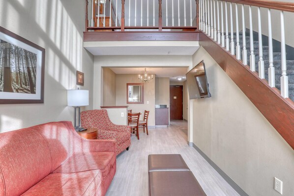 Amplia sala de estar con un sofá rojo, un sillón estampado y un banco de madera. Una escalera con barandilla de madera conduce a un nivel superior.