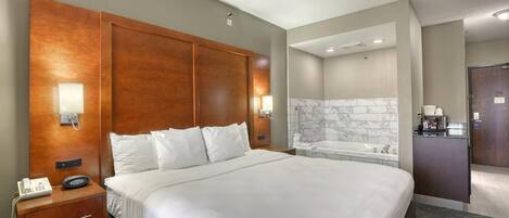 Une chambre d’hôtel dotée d’un grand lit, de tables de chevet, d’un téléphone, d’un miroir, d’une salle de bain avec baignoire et d’un espace bureau.