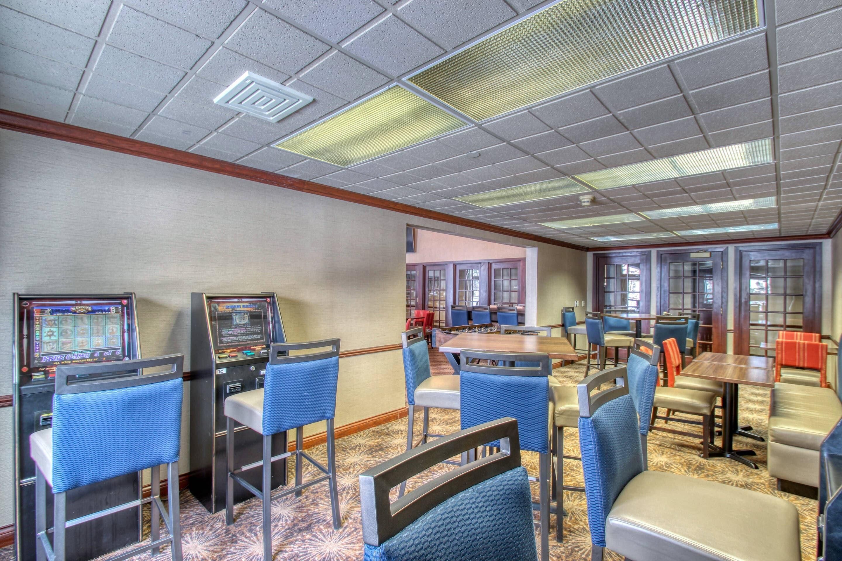 A hotel lobby with gaming machines, blue and beige chairs, and a carpeted floor.