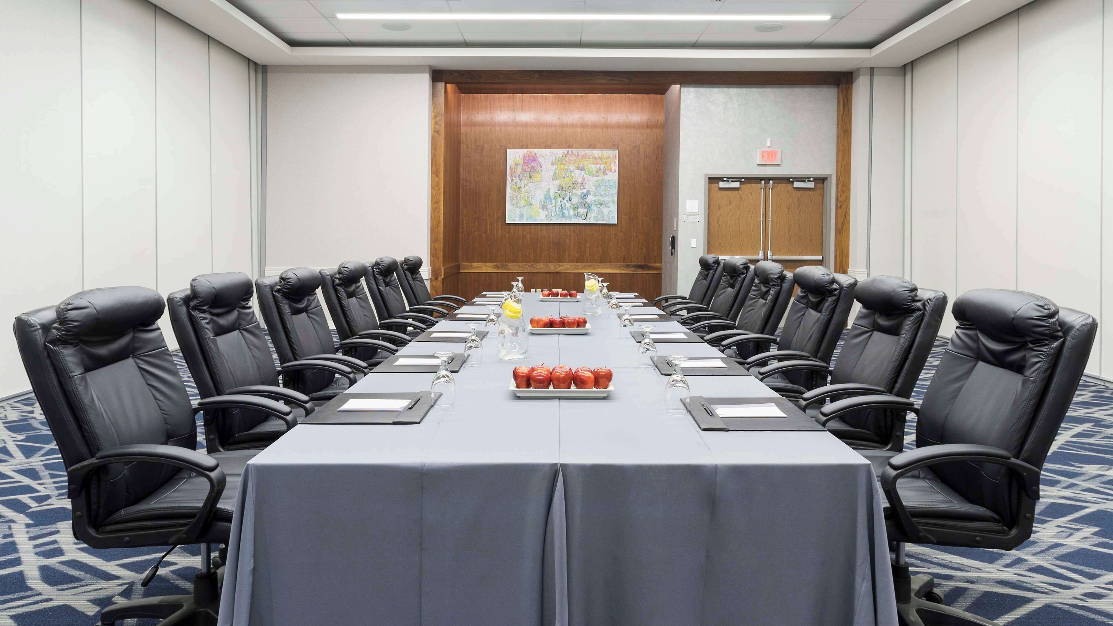 A conference room with a long table, black leather chairs, and a blue carpet.