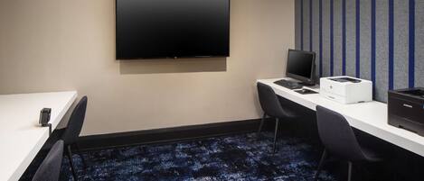 A conference room with a flat-screen TV, a desktop computer, a printer, and two chairs.