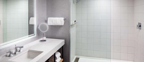 Un baño moderno con ducha de vidrio, un espejo grande y un lavamanos de mármol.