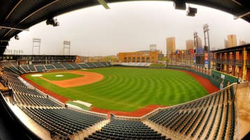 Un estadio de béisbol con varias secciones de asientos, un campo bien cuidado y edificios urbanos aledaños.