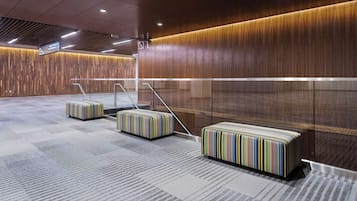 A modern lobby with a wooden wall, a glass elevator, and striped luggage on the floor.