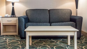 A hotel room with a grey sofa, a small table, two bedside lamps, a bedside telephone, and a patterned carpet. - Quality Inn Geneseo (Geneseo)