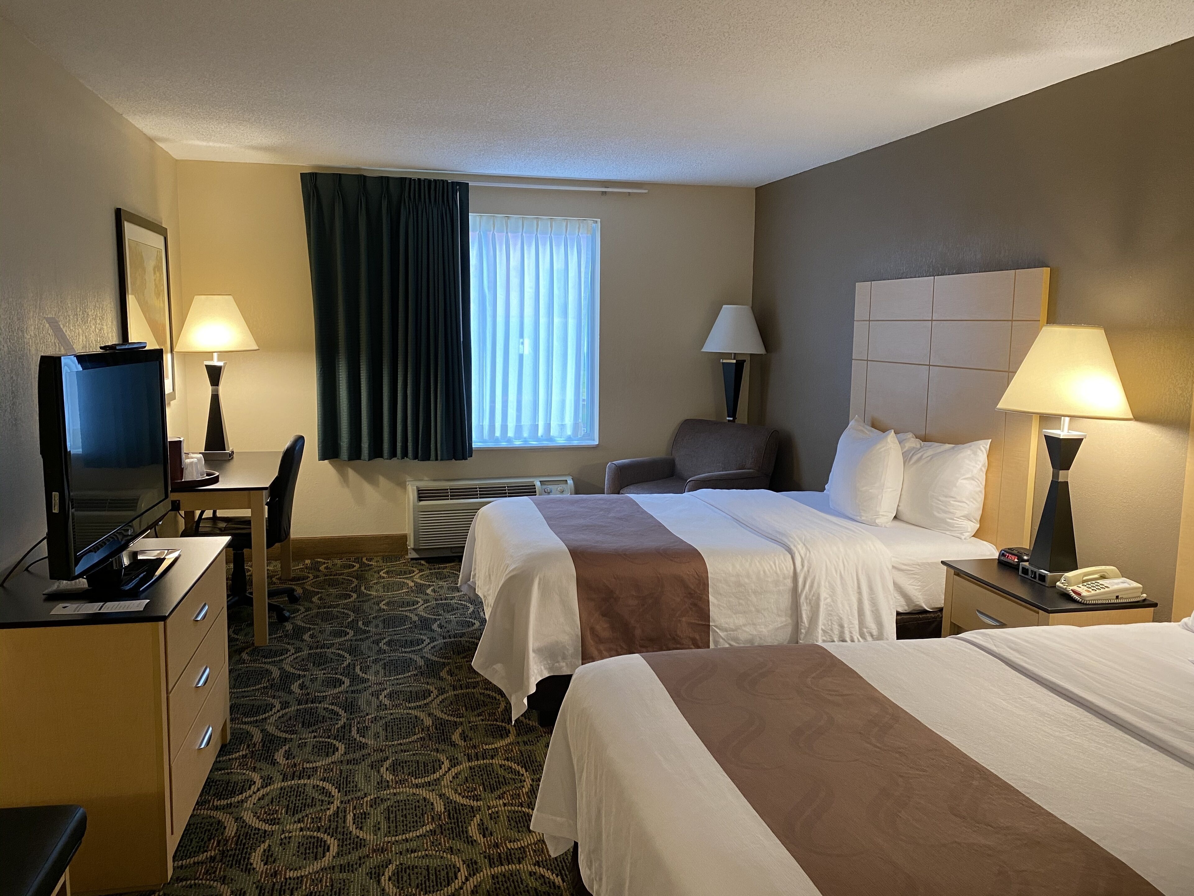 A hotel room with two beds, a desk with a computer, a chair, a TV, and two lamps.