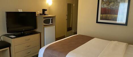 Habitación de hotel con cama, televisión, microondas, escritorio con cajones y un cuadro en la pared.