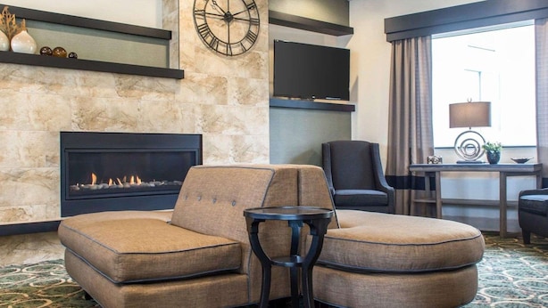 A hotel lobby with a fireplace, a sofa, a chair, a TV, and a window with curtains. - Quality Inn Geneseo (Geneseo)