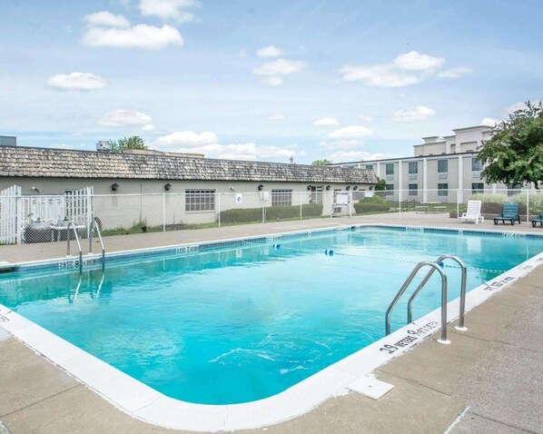 A swimming pool with clear blue water, surrounded by a white fence and a paved deck.