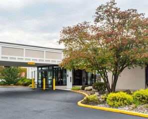 A modern building with a covered entrance, a landscaped area with shrubs and a tree, and a clear sky.