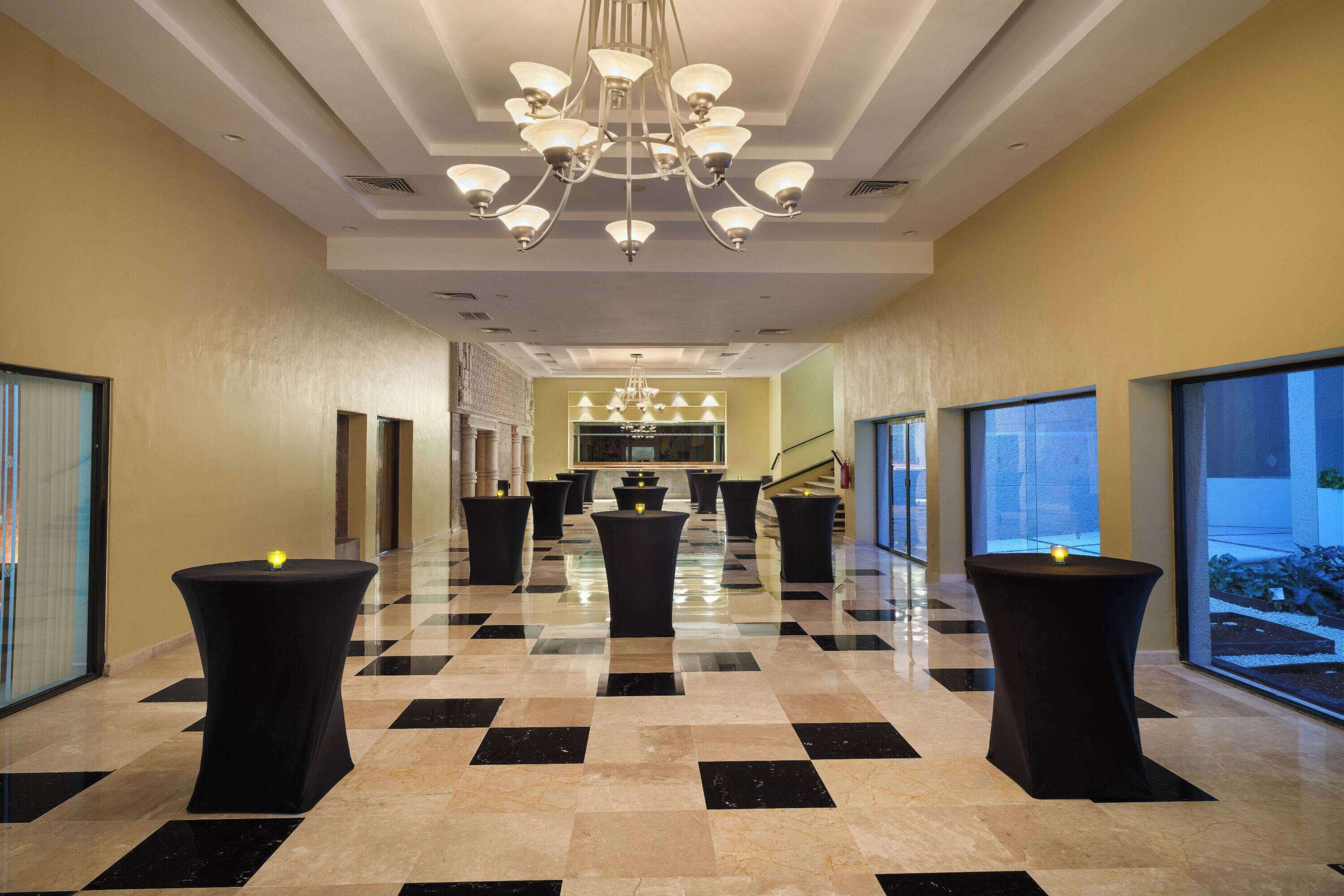 Un hall d’hôtel avec un sol à carreaux, des tables noires et un lustre.