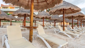 A beach with rows of white lounge chairs and thatched umbrellas.