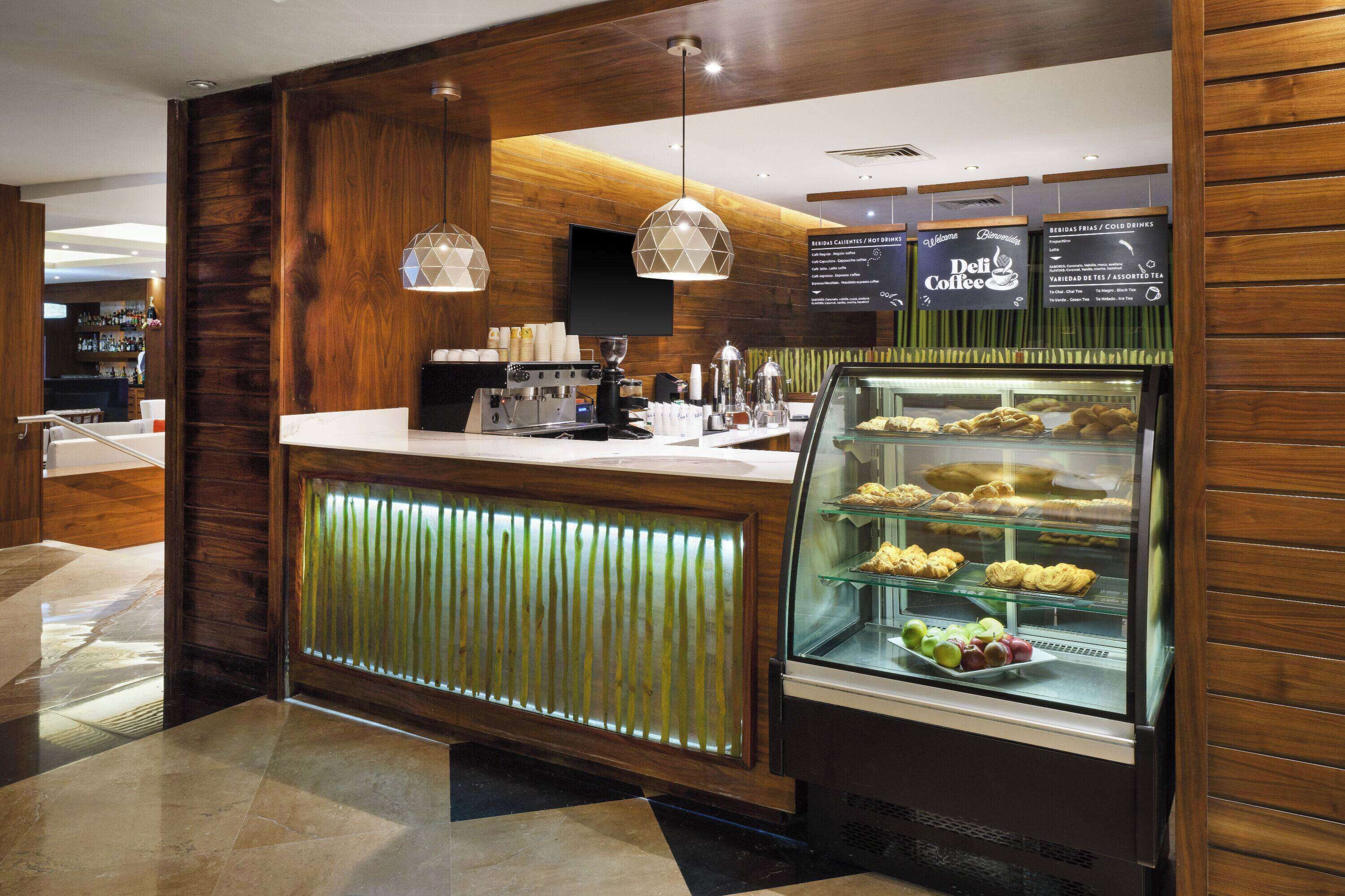 A modern coffee shop with a wooden interior, a counter with a coffee machine, and a display case with pastries.