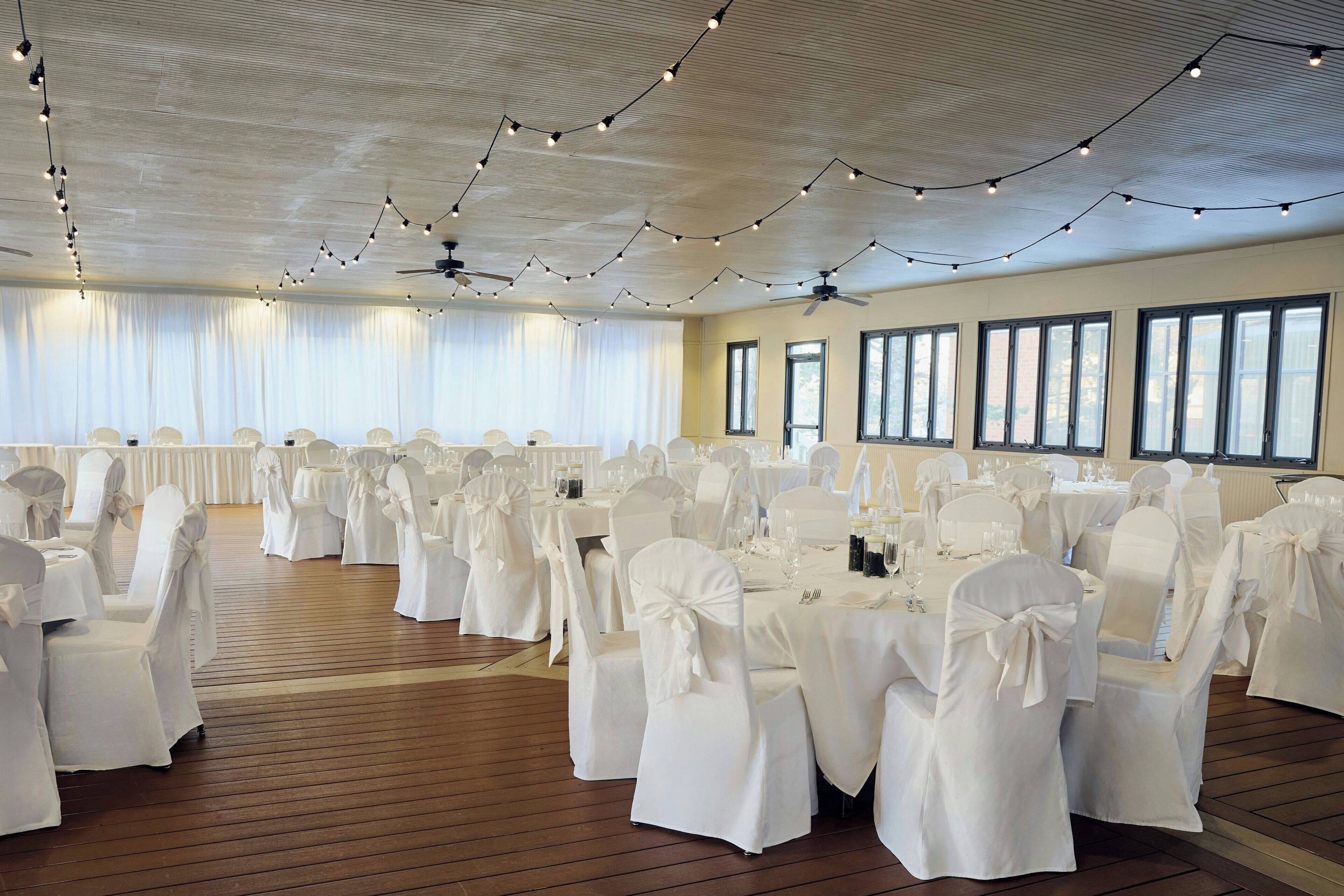 A banquet hall with round tables, white tablecloths, and chairs with bows.