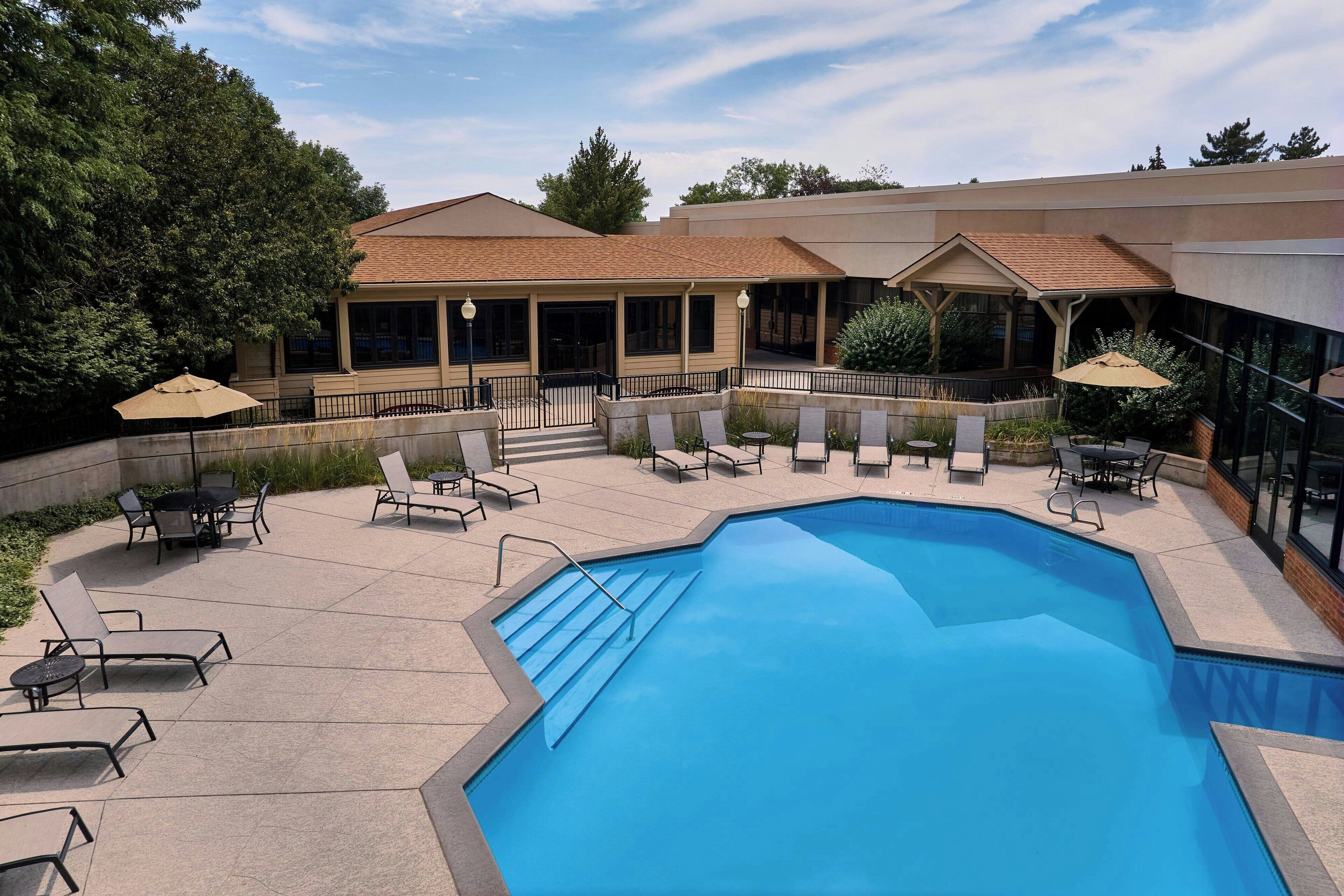 A swimming pool with lounge chairs and umbrellas, surrounded by a covered patio area with tables and chairs.