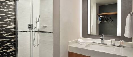 A modern bathroom with a glass-enclosed shower, a white sink with toiletries, and a large mirror.