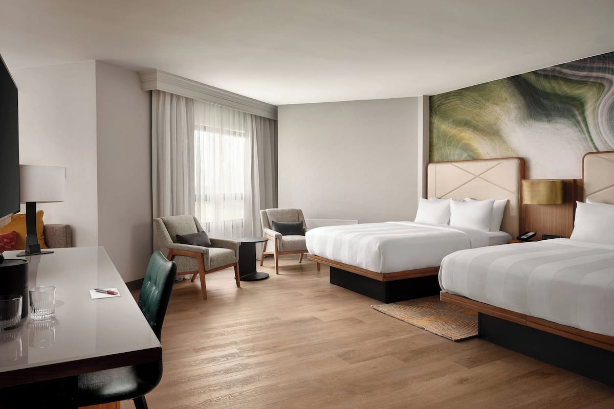 A hotel room with two beds, a desk, a chair, a small table, and a large abstract painting on the wall.