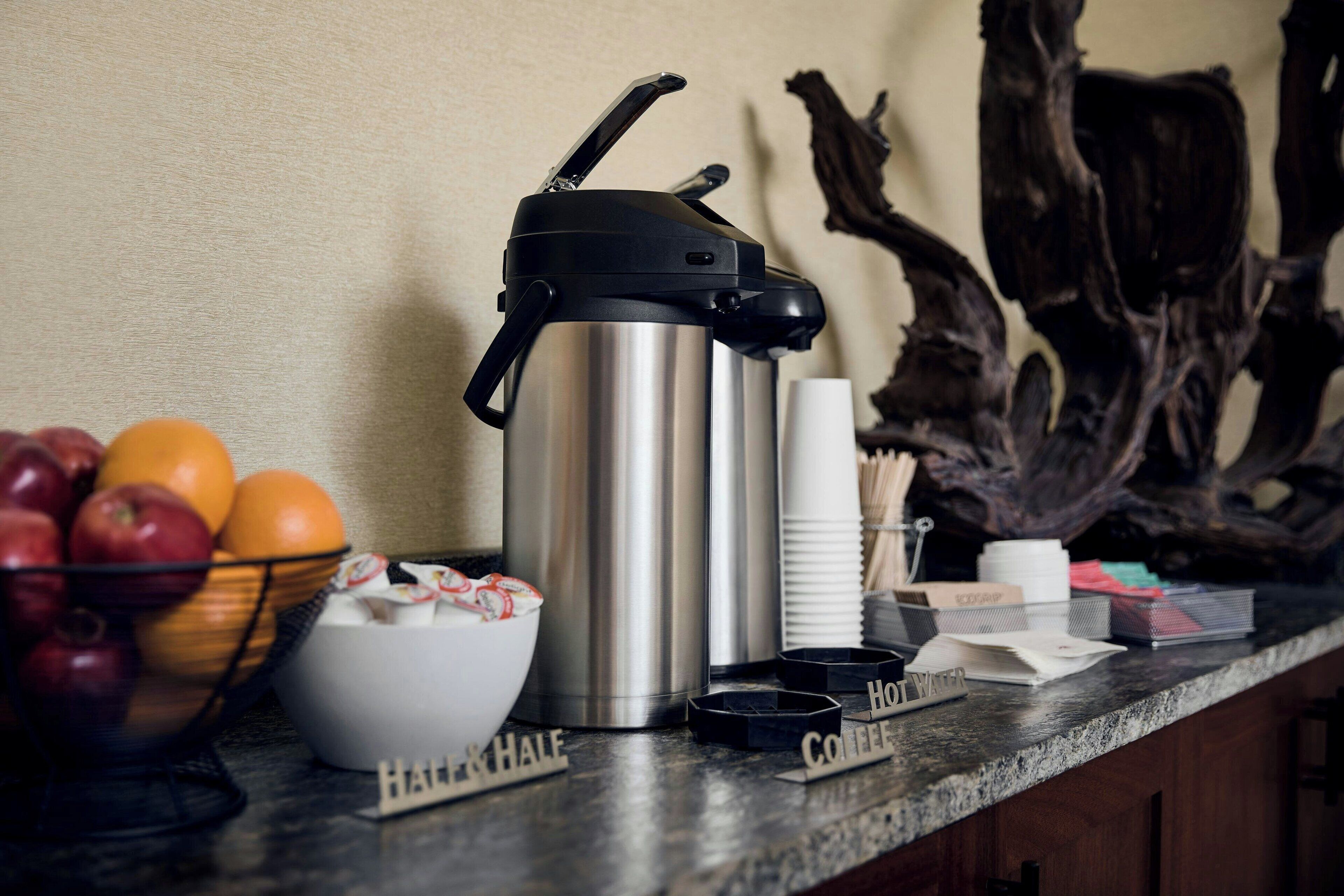 Una encimera de cocina con una botella de agua de acero inoxidable, un cuenco de fruta y una estación de café.
