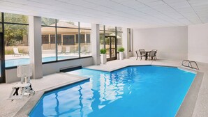 Ein Innenpool mit großen Glaswänden, einem Rettungsschwimmerstuhl und einem Tisch am Pool.