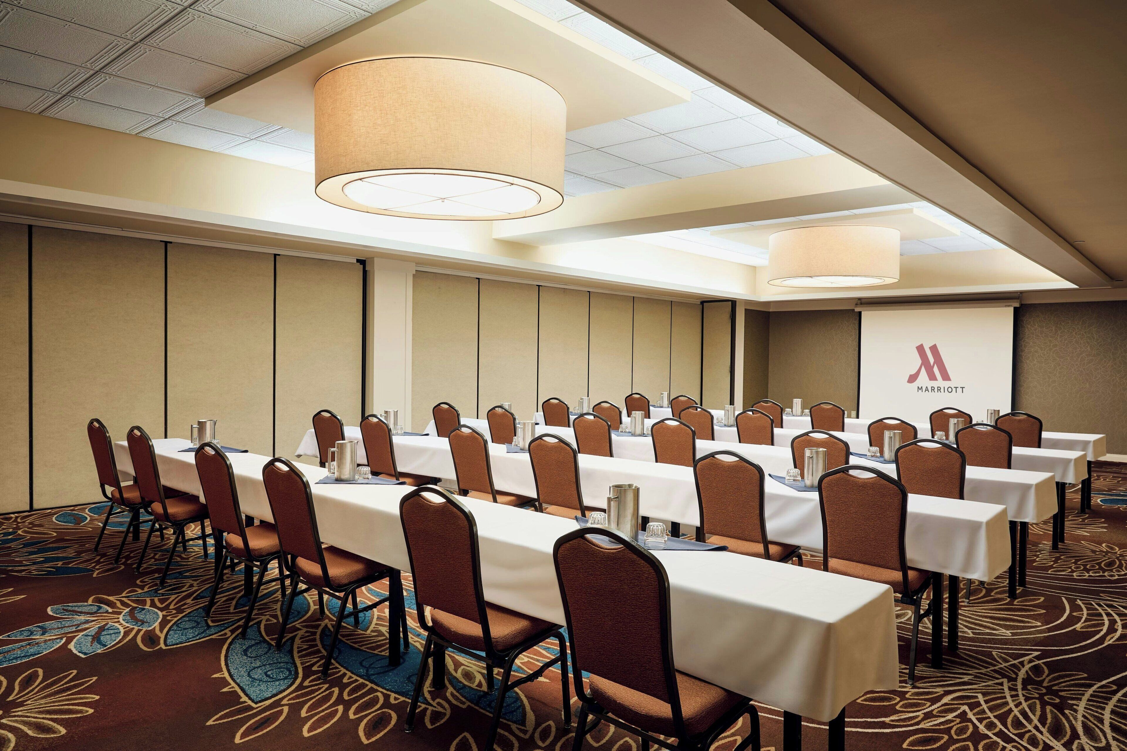 A conference room with long tables, chairs, and a presentation screen.