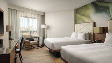 Habitación de hotel con dos camas, un escritorio, una silla y un ventanal con cortinas.