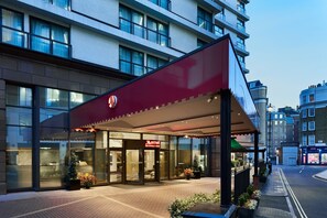 A Marriott hotel entrance with a red awning, large glass doors, and a Christmas tree. - London Marriott Hotel Marble Arch (London)