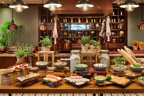Una mesa de buffet con diversos alimentos y al fondo, una cocina con utensilios y frascos colgados.