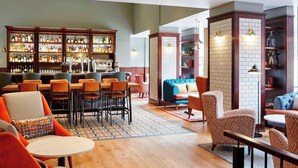 A bar area with shelves of bottles, a seating area with chairs and tables, and a blue sofa. - London Marriott Hotel Marble Arch (London)