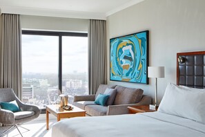 A hotel room with a large bed, a sofa, a chair, a table, and a painting on the wall.