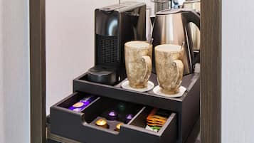 Een koffieapparaat met twee kopjes en een lade met diverse spullen.