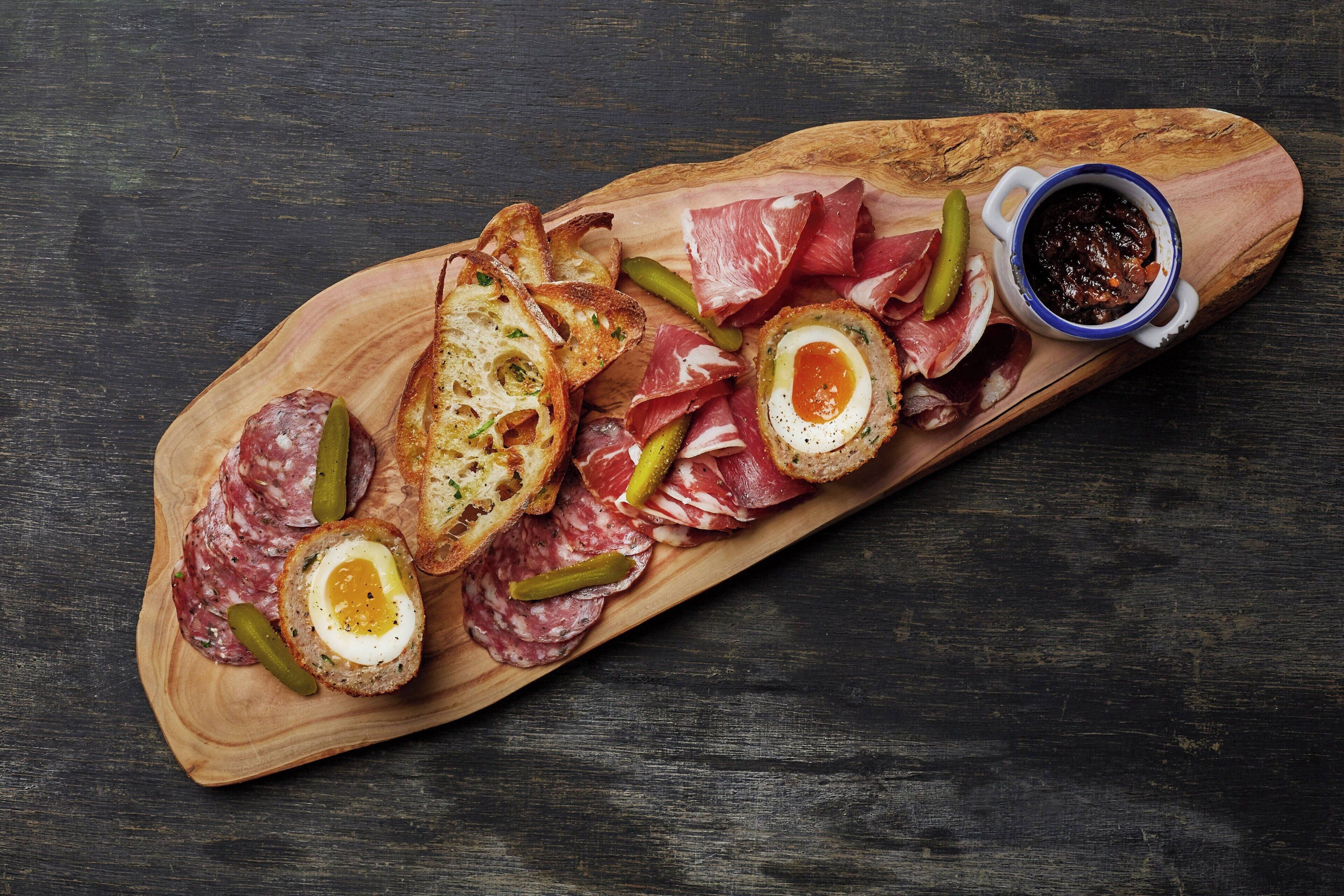 Un tagliere di legno con salumi assortiti, sottaceti e fette di pane.