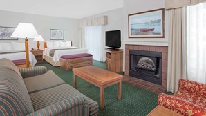A hotel room with a bed, a sofa, a table, a TV, a fireplace, and a painting on the wall.
