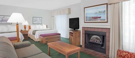 A hotel room with a bed, a sofa, a table, a TV, a fireplace, and a painting on the wall.