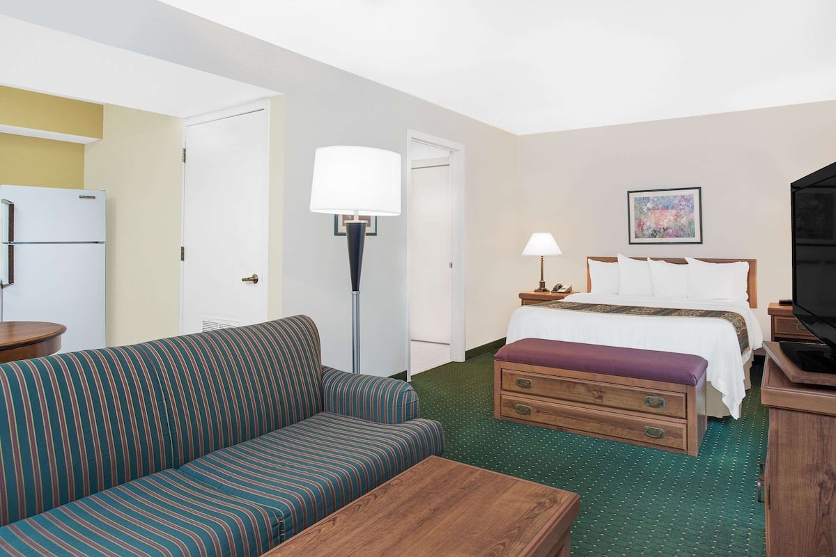 A hotel room with a bed, a sofa, a desk, a lamp, a television, and a refrigerator.