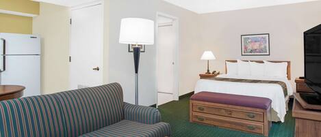 A hotel room with a bed, a sofa, a desk, a lamp, a television, and a refrigerator.