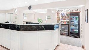 A reception area with a marble counter, a clock, and a 'Shacks Drinks' refrigerator stocked with beverages.