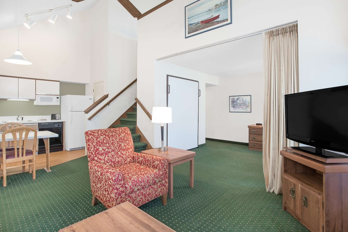 A compact living space with a dining area, a sofa, a TV, and a staircase leading to an upper level.