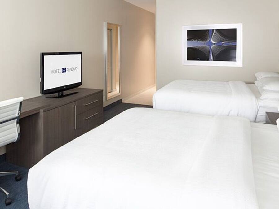 A hotel room with two beds, a desk with a computer, a chair, and artwork on the walls.