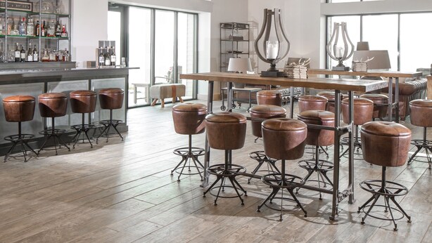 A spacious bar area with high ceilings, large windows, and multiple bar stools. - Hotel Renovo Des Moines Urbandale,Tapestry Collection Hilton (Urbandale)