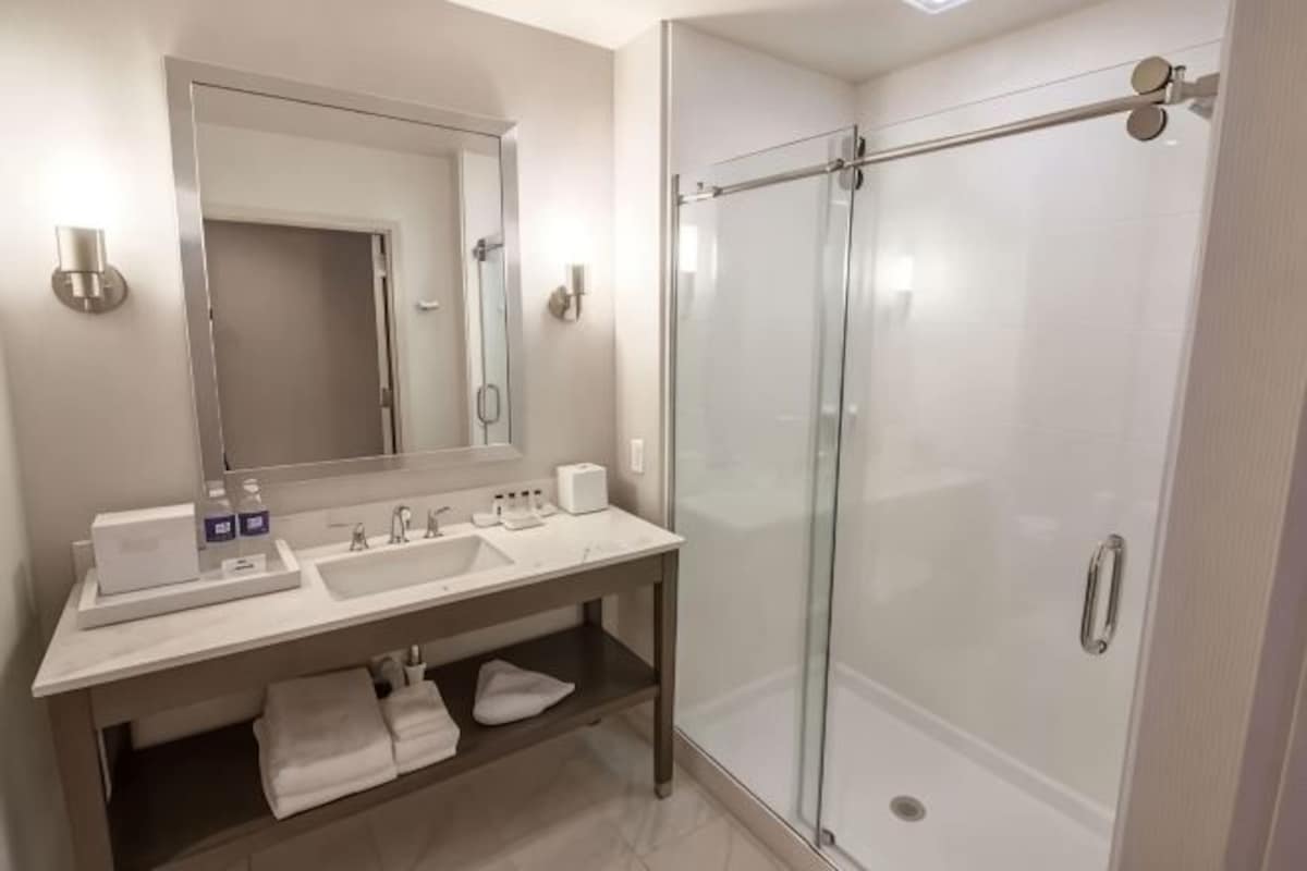 A modern bathroom with a glass-enclosed shower, a large mirror, and a vanity with a sink and towel rack.