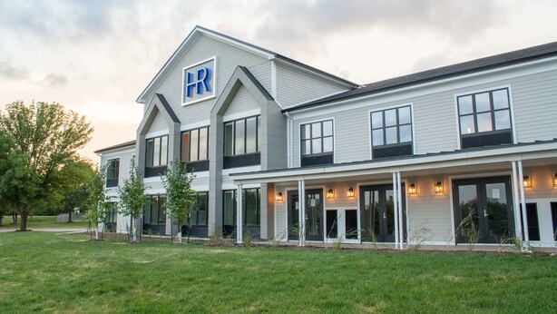 A modern two-story building with a prominent 'HR' sign on the roof, large windows, and a covered front porch area. - Hotel Renovo Des Moines Urbandale,Tapestry Collection Hilton (Urbandale)