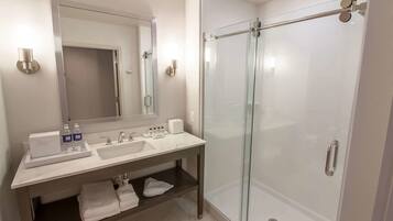 Un baño moderno con ducha envuelta en vidrio, un espejo grande y un tocador con dos lavamanos y un perchero para toallas.